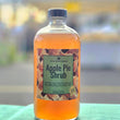 Load image into Gallery viewer, A bottle of Apple Pie Shrub by Apple State Vinegar, filled with an amber-colored liquid, set on a green cloth with a blurred outdoor background.
