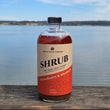 Load image into Gallery viewer, A bottle of Apple State Vinegar Strawberry &amp; Rhubarb Shrub, sits on a wooden deck with distant shoreline in the background. The bottle has a black cap and a cream and red label with black text.

